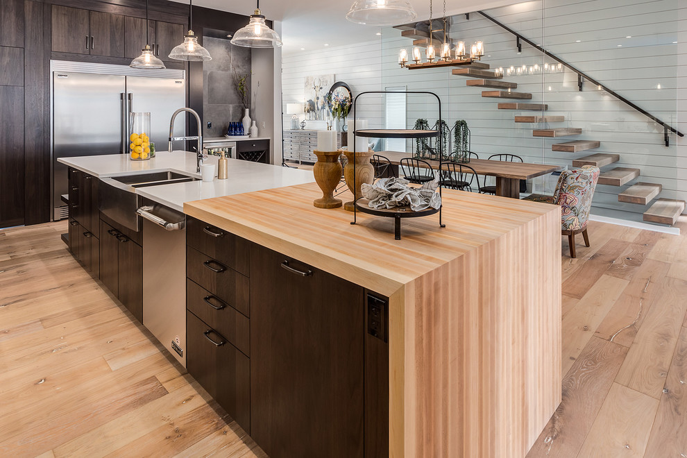 Inspiration for a large country l-shaped eat-in kitchen in Calgary with an undermount sink, flat-panel cabinets, dark wood cabinets, quartz benchtops, white splashback, subway tile splashback, stainless steel appliances, light hardwood floors, with island and beige floor.