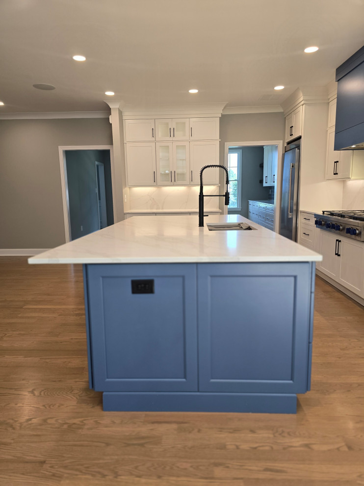 Large minimalist l-shaped medium tone wood floor and brown floor kitchen photo with an undermount sink, shaker cabinets, white cabinets, quartz countertops, gray backsplash, subway tile backsplash, stainless steel appliances, an island and white countertops