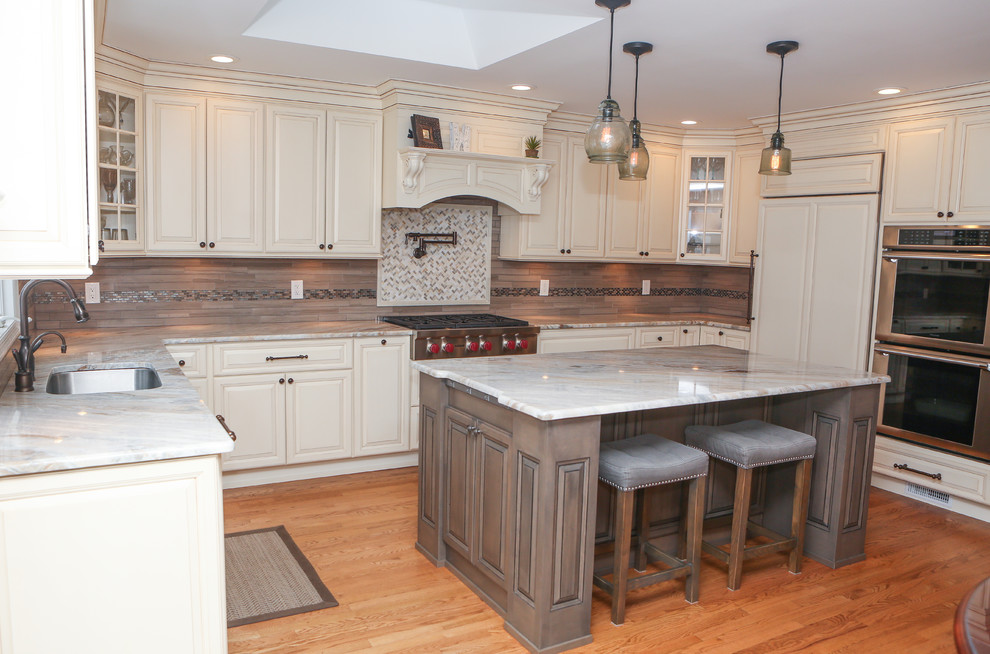 Large transitional u-shaped light wood floor eat-in kitchen photo in Newark with an undermount sink, raised-panel cabinets, distressed cabinets, granite countertops, brown backsplash, mosaic tile backsplash, stainless steel appliances and an island