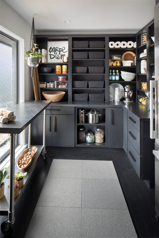 This is an example of an expansive transitional l-shaped kitchen pantry in Indianapolis with flat-panel cabinets, black cabinets, solid surface benchtops, stainless steel appliances, dark hardwood floors, with island and black floor.