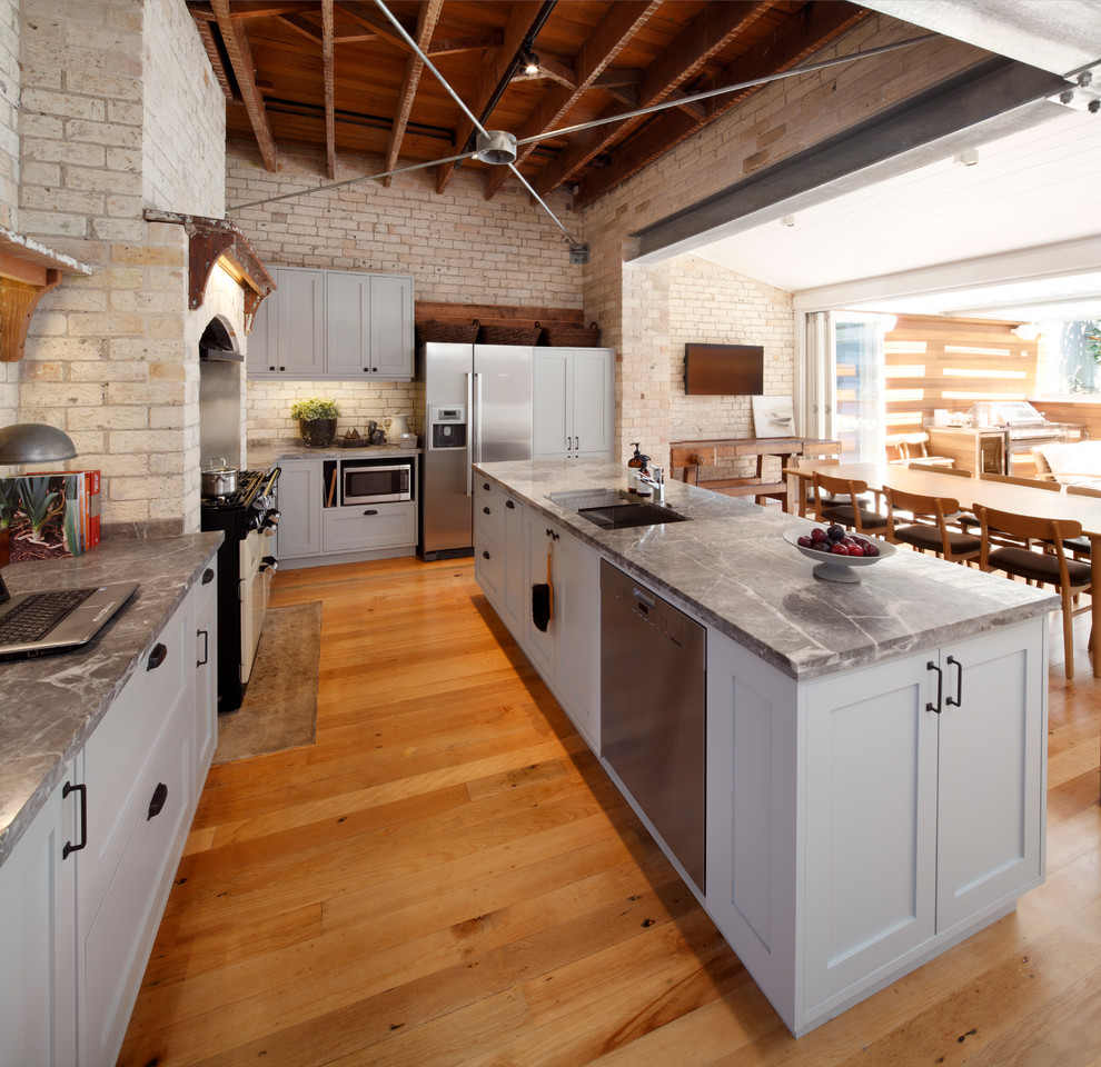 Inspiration for an industrial l-shaped eat-in kitchen in Sydney with an undermount sink, grey cabinets, marble benchtops, beige splashback, stainless steel appliances, black walls, medium hardwood floors and with island.
