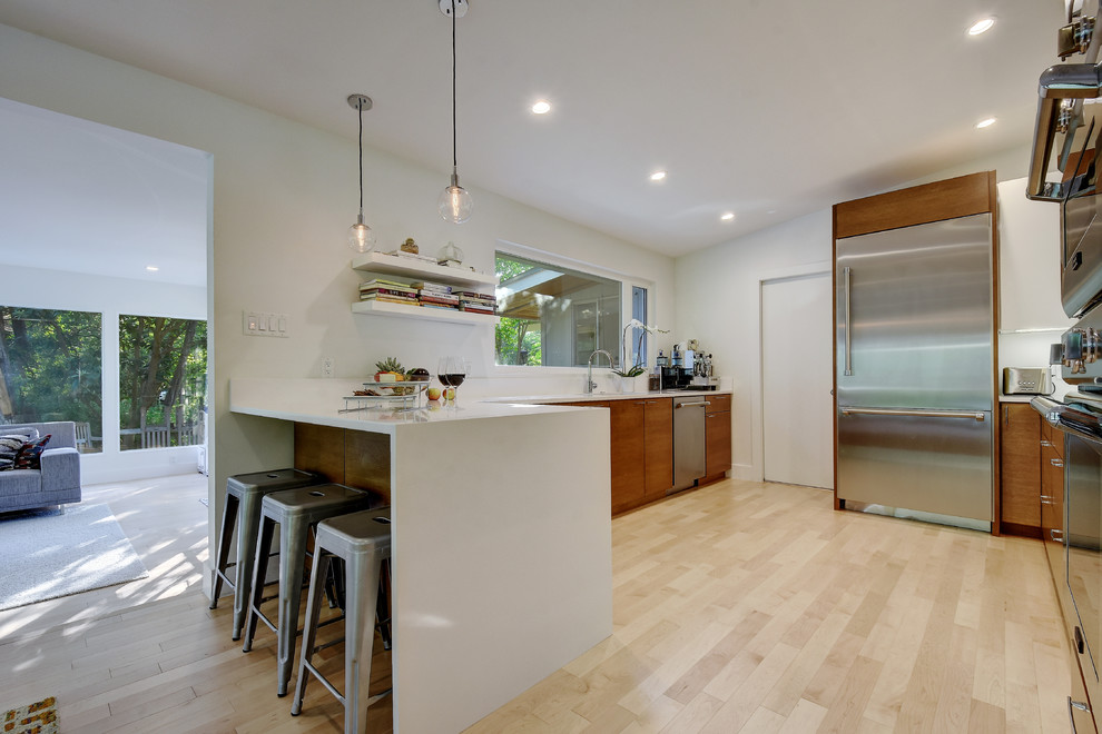 Inspiration for a large midcentury galley eat-in kitchen in Austin with an undermount sink, flat-panel cabinets, medium wood cabinets, quartz benchtops, white splashback, glass sheet splashback, stainless steel appliances and light hardwood floors.