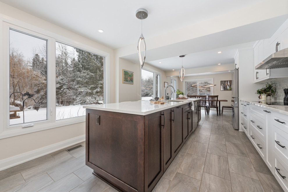 This is an example of a modern kitchen/diner in Ottawa with an island, a submerged sink, shaker cabinets, brown cabinets, engineered stone countertops, grey splashback, stainless steel appliances, ceramic flooring and white worktops.