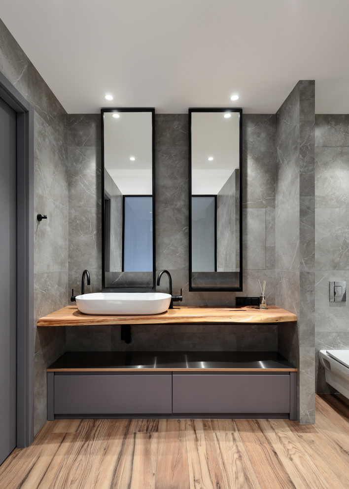 This is an example of a mid-sized scandinavian master bathroom in Saint Petersburg with flat-panel cabinets, grey cabinets, a freestanding tub, an alcove shower, a wall-mount toilet, gray tile, porcelain tile, grey walls, wood-look tile, a vessel sink, wood benchtops, brown floor, a shower curtain, brown benchtops, a single vanity and a freestanding vanity.