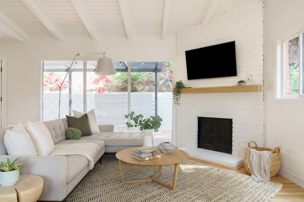 Small midcentury open concept living room in Los Angeles with white walls, medium hardwood floors, a corner fireplace, a brick fireplace surround, a corner tv, brown floor and timber.