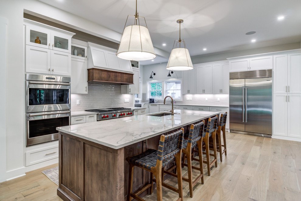Inspiration for a large transitional kitchen in Cleveland with an undermount sink, shaker cabinets, white cabinets, quartzite benchtops, grey splashback, ceramic splashback, stainless steel appliances, light hardwood floors, with island and white benchtop.