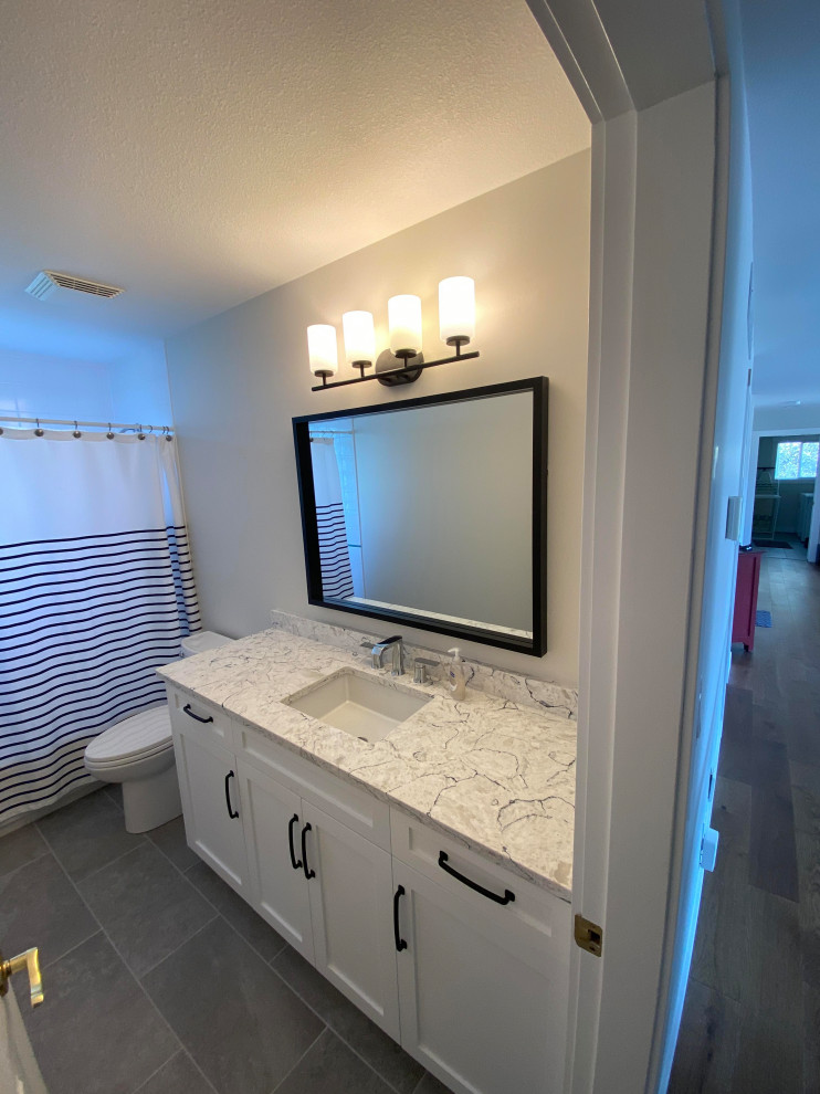 Tub/shower combo - mid-sized transitional single-sink tub/shower combo idea with shaker cabinets, a one-piece toilet, gray walls, an undermount sink and a built-in vanity