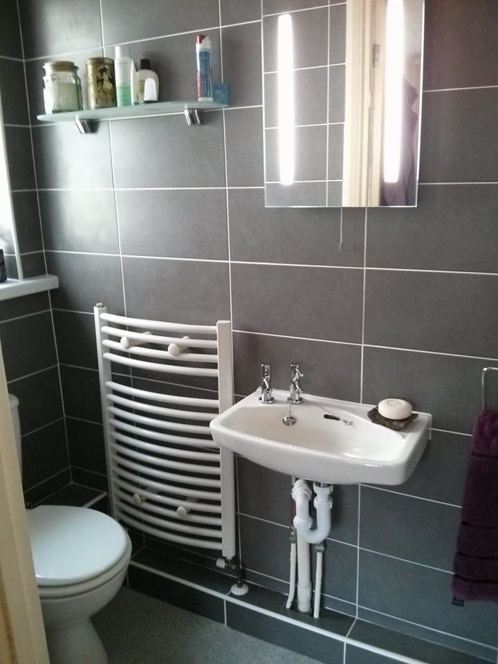 Photo of a small contemporary 3/4 bathroom in Essex with a wall-mount sink, beaded inset cabinets, an alcove shower, a two-piece toilet, gray tile, ceramic tile, grey walls and mosaic tile floors.