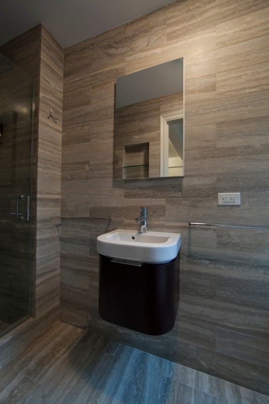 This is an example of a modern master bathroom in New York with a pedestal sink, flat-panel cabinets, dark wood cabinets, multi-coloured tile, stone tile, multi-coloured walls and travertine floors.