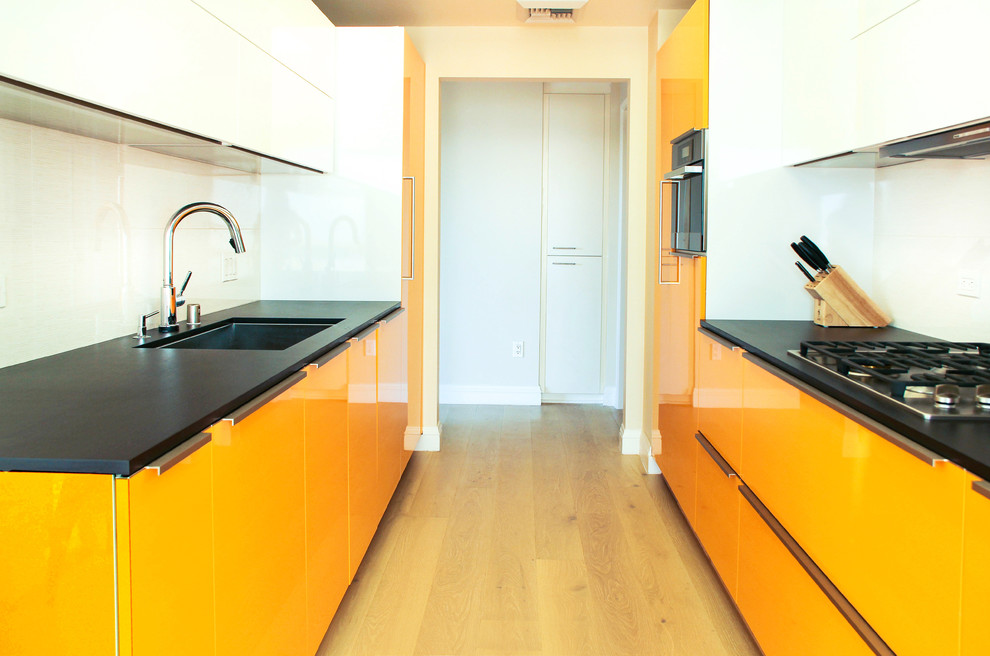 Design ideas for a small modern single-wall eat-in kitchen in Los Angeles with a drop-in sink, flat-panel cabinets, orange cabinets, quartz benchtops, black splashback, porcelain splashback, stainless steel appliances, light hardwood floors and no island.