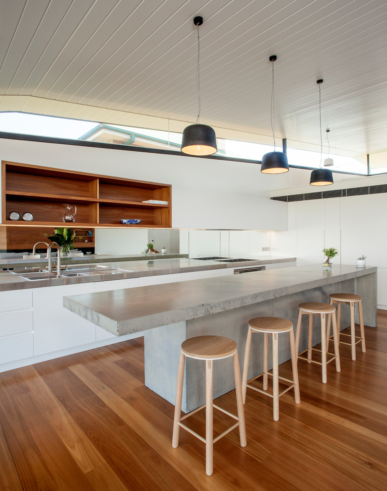 Large contemporary galley open plan kitchen in Sydney with white cabinets, concrete benchtops, stainless steel appliances, medium hardwood floors, with island, a double-bowl sink, flat-panel cabinets, metallic splashback, mirror splashback and brown floor.