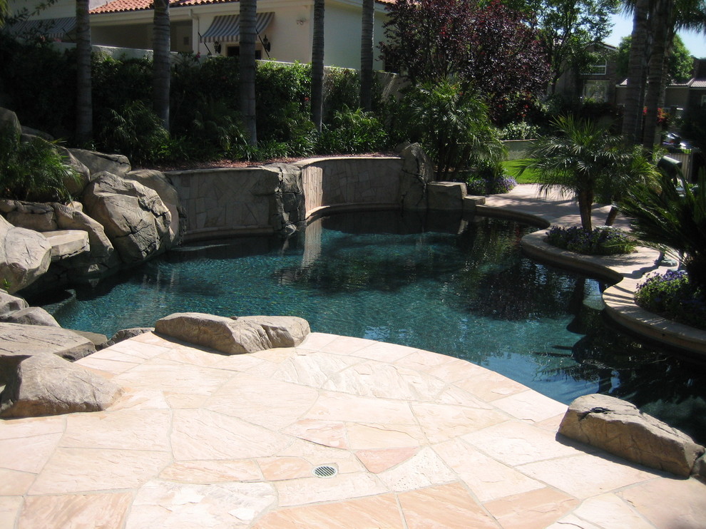 This is an example of a mid-sized country backyard custom-shaped pool in Orange County with a water slide and natural stone pavers.