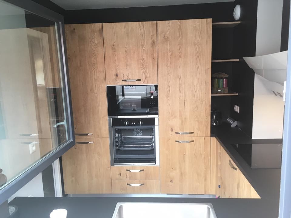 Mid-sized contemporary l-shaped open plan kitchen in Lille with an undermount sink, recessed-panel cabinets, light wood cabinets, solid surface benchtops, black splashback, panelled appliances, cement tiles, no island and grey floor.