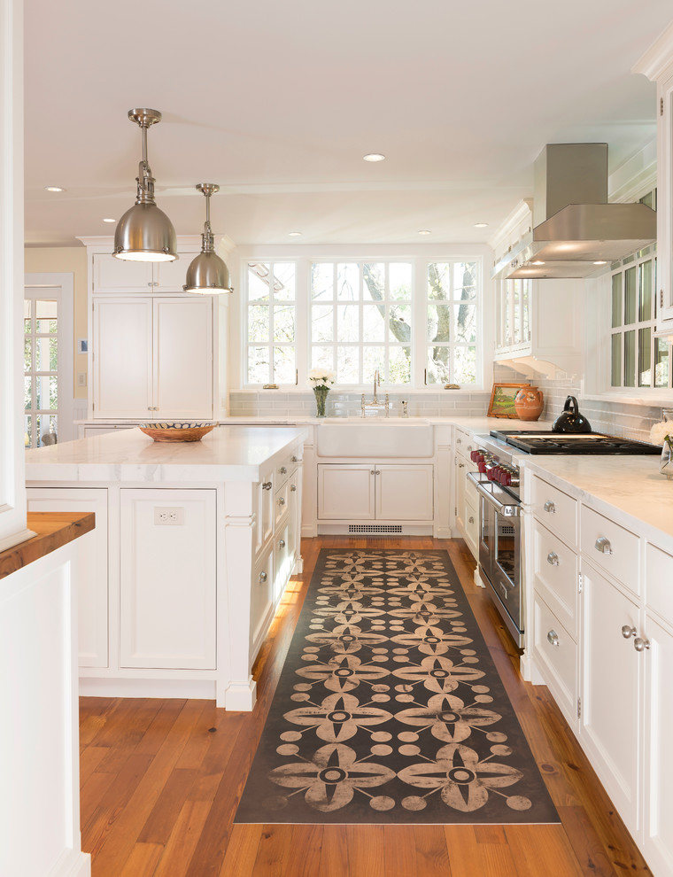 Elegant u-shaped medium tone wood floor kitchen photo in DC Metro with a farmhouse sink, shaker cabinets, white cabinets, white backsplash, subway tile backsplash, stainless steel appliances and an island