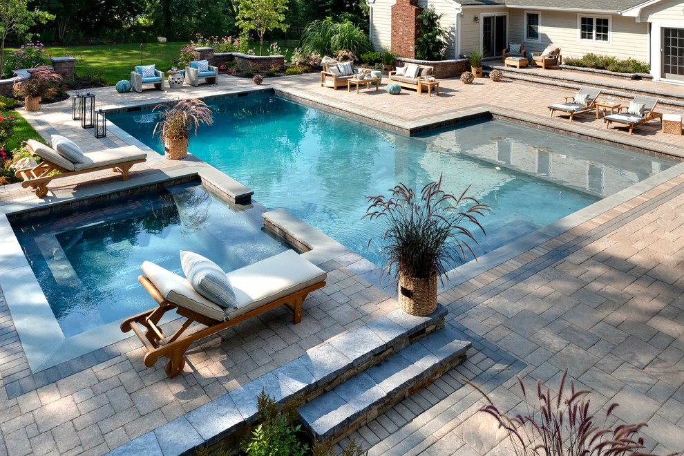 Large traditional backyard custom-shaped lap pool in Philadelphia with a hot tub and natural stone pavers.