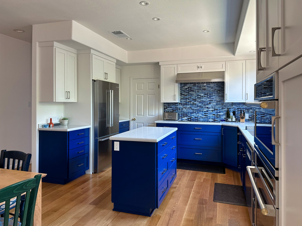 Idéer för ett litet eklektiskt vit kök och matrum, med en undermonterad diskho, skåp i shakerstil, blå skåp, bänkskiva i kvarts, blått stänkskydd, stänkskydd i glaskakel, rostfria vitvaror, mellanmörkt trägolv, en köksö och brunt golv