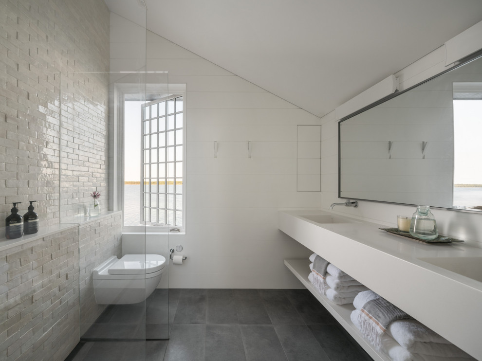 Inspiration for a coastal ensuite bathroom in Other with open cabinets, white cabinets, a walk-in shower, a wall mounted toilet, white tiles, ceramic tiles, white walls, ceramic flooring, quartz worktops, grey floors, an open shower, white worktops, double sinks, a floating vanity unit, a vaulted ceiling and panelled walls.