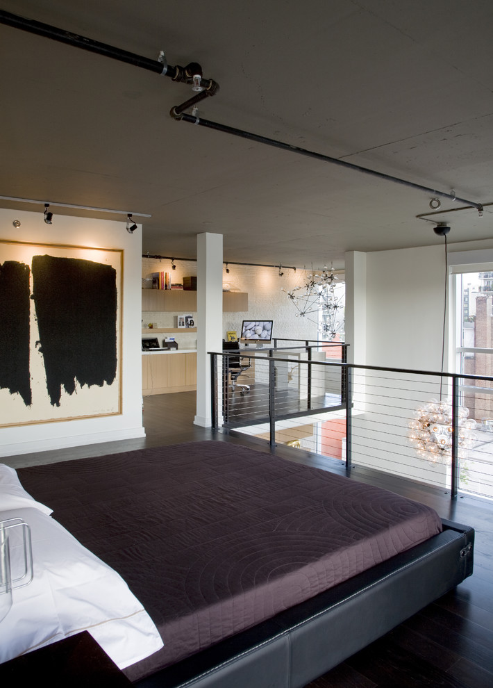 This is an example of an industrial loft-style bedroom in DC Metro with white walls, dark hardwood floors and no fireplace.