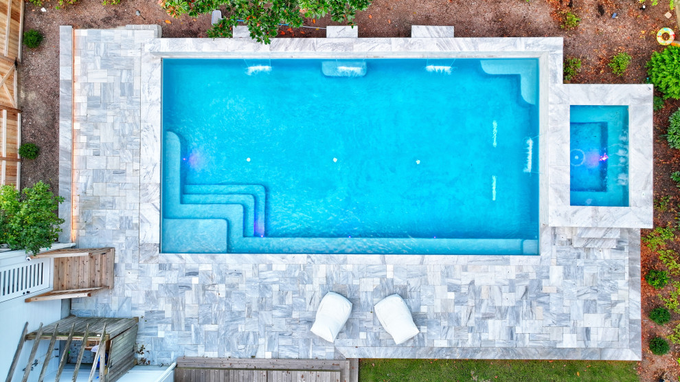 Modern inredning av en stor rektangulär pool på baksidan av huset, med spabad och naturstensplattor