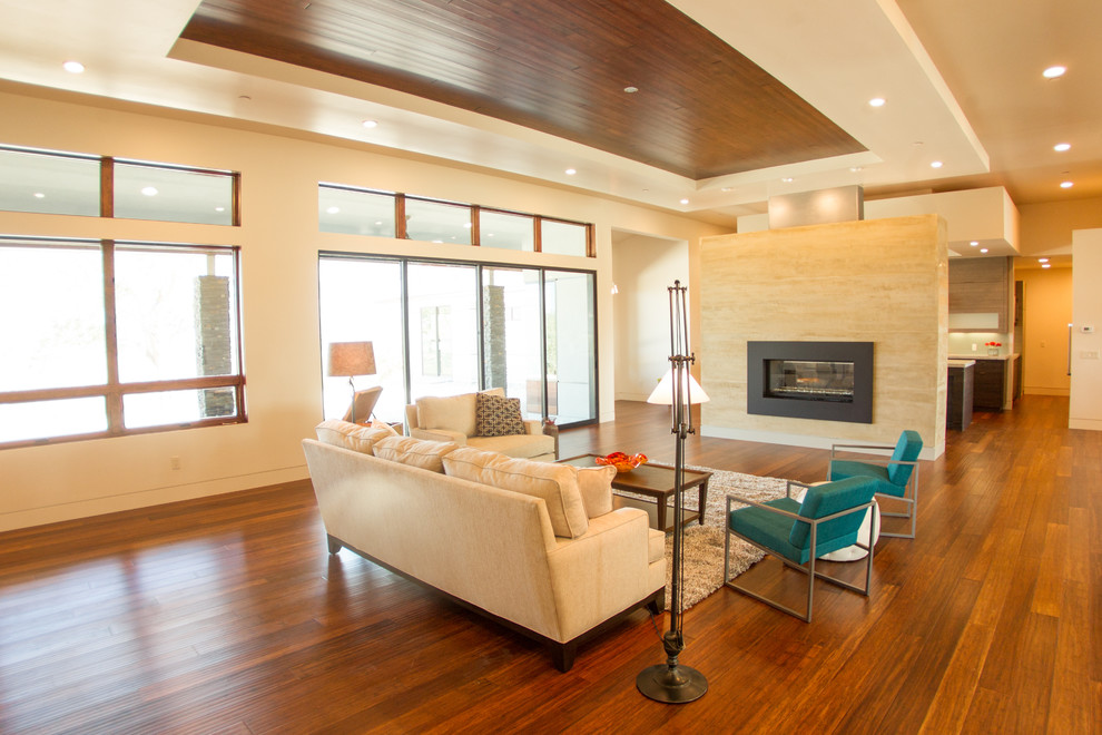 This is an example of a large contemporary open concept living room in San Luis Obispo with beige walls, bamboo floors, a two-sided fireplace, a plaster fireplace surround and a wall-mounted tv.