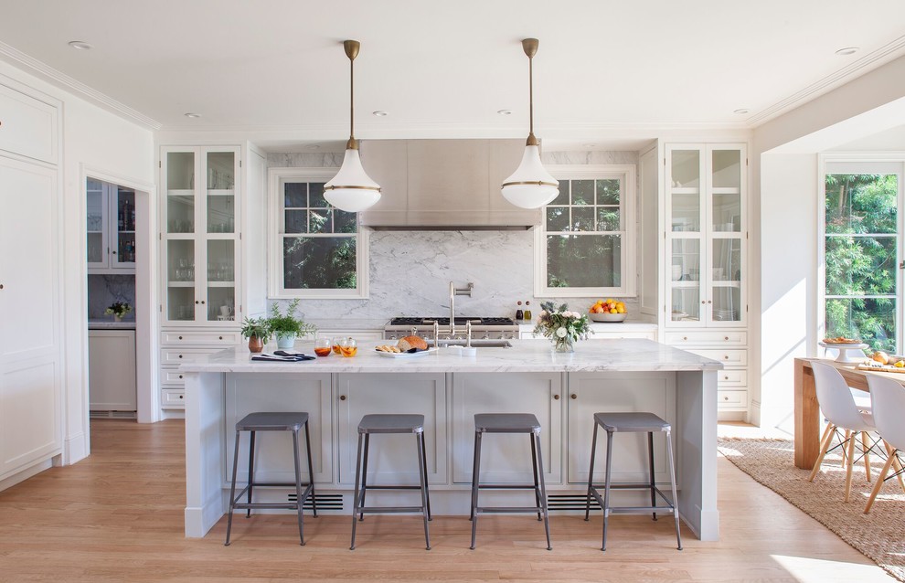 Inspiration for a mid-sized transitional l-shaped eat-in kitchen in Los Angeles with an undermount sink, glass-front cabinets, white cabinets, marble benchtops, white splashback, stone slab splashback, stainless steel appliances, light hardwood floors and with island.