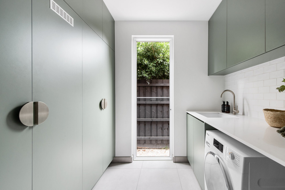 Inspiration for a medium sized contemporary galley separated utility room in Melbourne with flat-panel cabinets, green cabinets, limestone worktops, white worktops, a built-in sink, white splashback, metro tiled splashback, white walls, porcelain flooring, an integrated washer and dryer and grey floors.