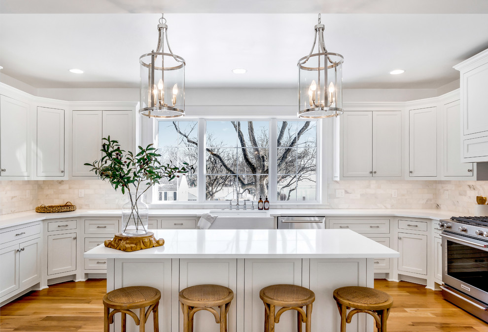 Inspiration for a large country u-shaped open plan kitchen in Kansas City with grey splashback, ceramic splashback, a farmhouse sink, shaker cabinets, white cabinets, stainless steel appliances, medium hardwood floors, with island, brown floor and white benchtop.