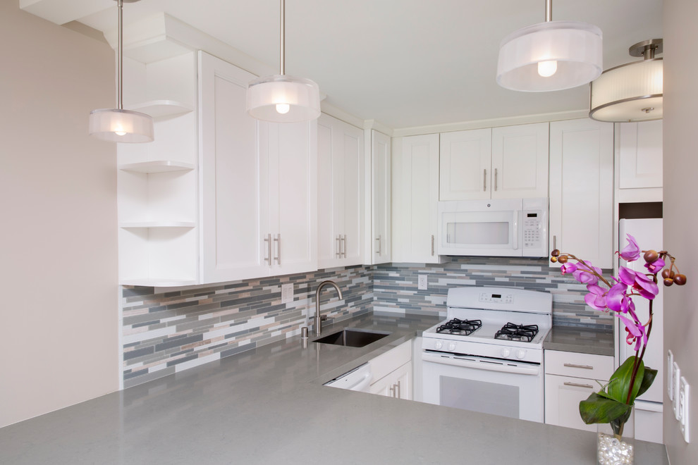 Photo of a transitional u-shaped kitchen in Hawaii with a single-bowl sink, shaker cabinets, white cabinets, grey splashback, mosaic tile splashback, white appliances, porcelain floors, no island and grey floor.