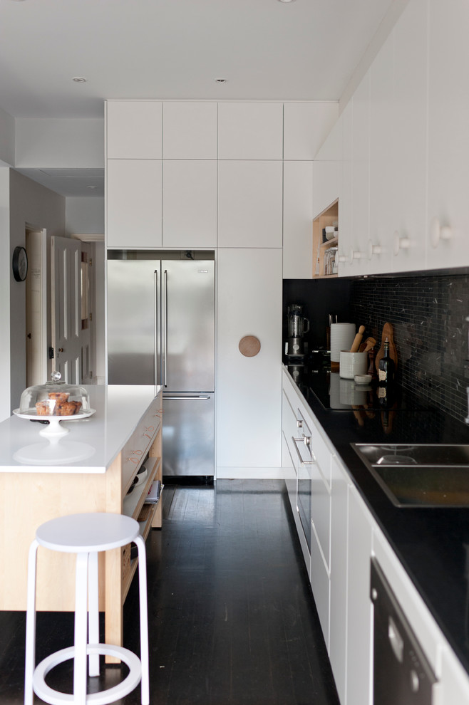 Scandinavian kitchen in Sydney with a drop-in sink, black splashback, mosaic tile splashback, stainless steel appliances, white cabinets, flat-panel cabinets and black floor.