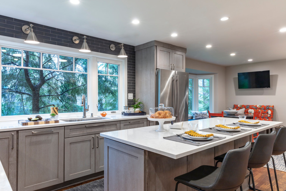 Example of a trendy u-shaped medium tone wood floor and brown floor eat-in kitchen design with an undermount sink, shaker cabinets, gray cabinets, quartz countertops, gray backsplash, ceramic backsplash, stainless steel appliances, an island and gray countertops