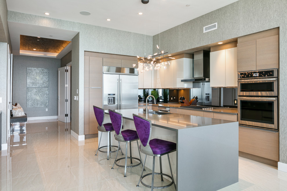 Inspiration for a medium sized contemporary l-shaped open plan kitchen in Tampa with a submerged sink, flat-panel cabinets, light wood cabinets, engineered stone countertops, grey splashback, mirror splashback, stainless steel appliances, porcelain flooring, an island, beige floors and grey worktops.