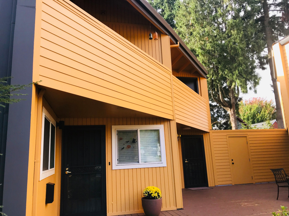 Стильный дизайн: двухэтажный, оранжевый многоквартирный дом среднего размера с облицовкой из ЦСП, плоской крышей, крышей из смешанных материалов, коричневой крышей и отделкой планкеном - последний тренд