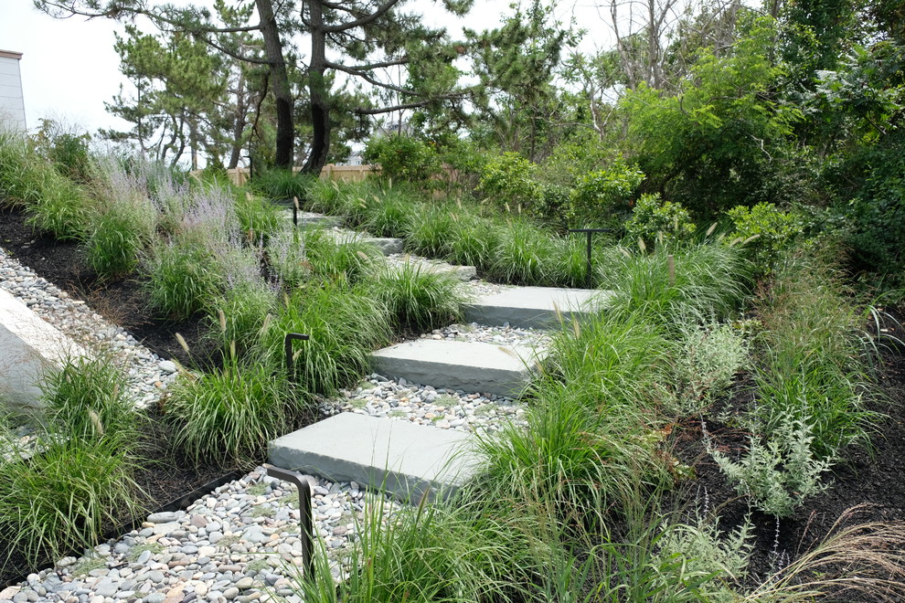 Large modern sloped full sun xeriscape in Boston with a garden path and natural stone pavers for summer.