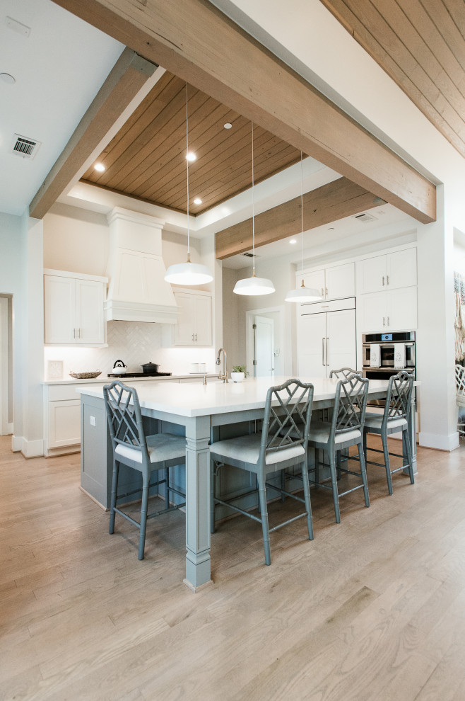 Inspiration for a transitional l-shaped kitchen in Houston with a farmhouse sink, shaker cabinets, white cabinets, panelled appliances, light hardwood floors, with island, beige floor, white benchtop and wood.