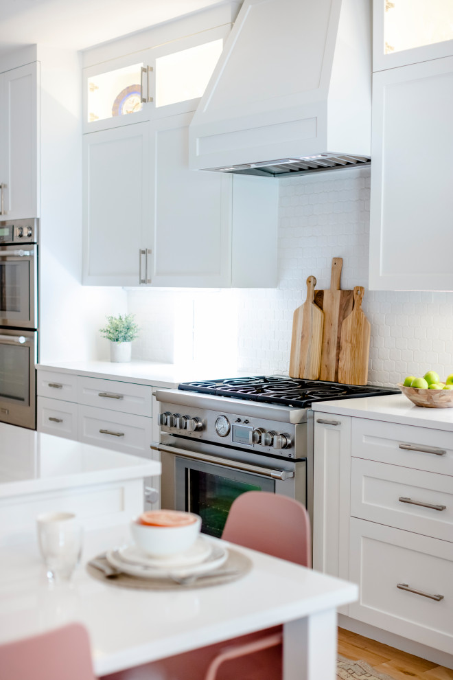 Inspiration for a large transitional l-shaped light wood floor and brown floor eat-in kitchen remodel in Austin with a single-bowl sink, shaker cabinets, white cabinets, quartz countertops, white backsplash, ceramic backsplash, stainless steel appliances, an island and white countertops