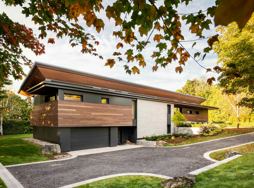 Photo of a large contemporary two-storey black house exterior in Toronto with mixed siding, a shed roof, a metal roof, a black roof and board and batten siding.