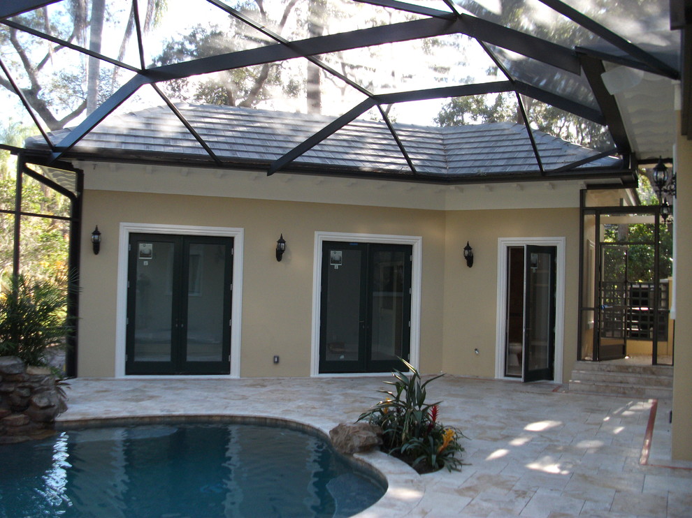 This is an example of a mid-sized traditional backyard custom-shaped pool in Tampa with a pool house and stamped concrete.