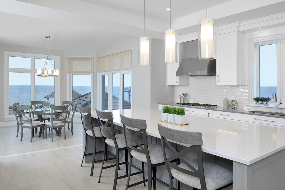 Inspiration for a large transitional l-shaped kitchen in Toronto with an undermount sink, recessed-panel cabinets, white cabinets, quartz benchtops, white splashback, subway tile splashback, white appliances, light hardwood floors, with island and brown floor.