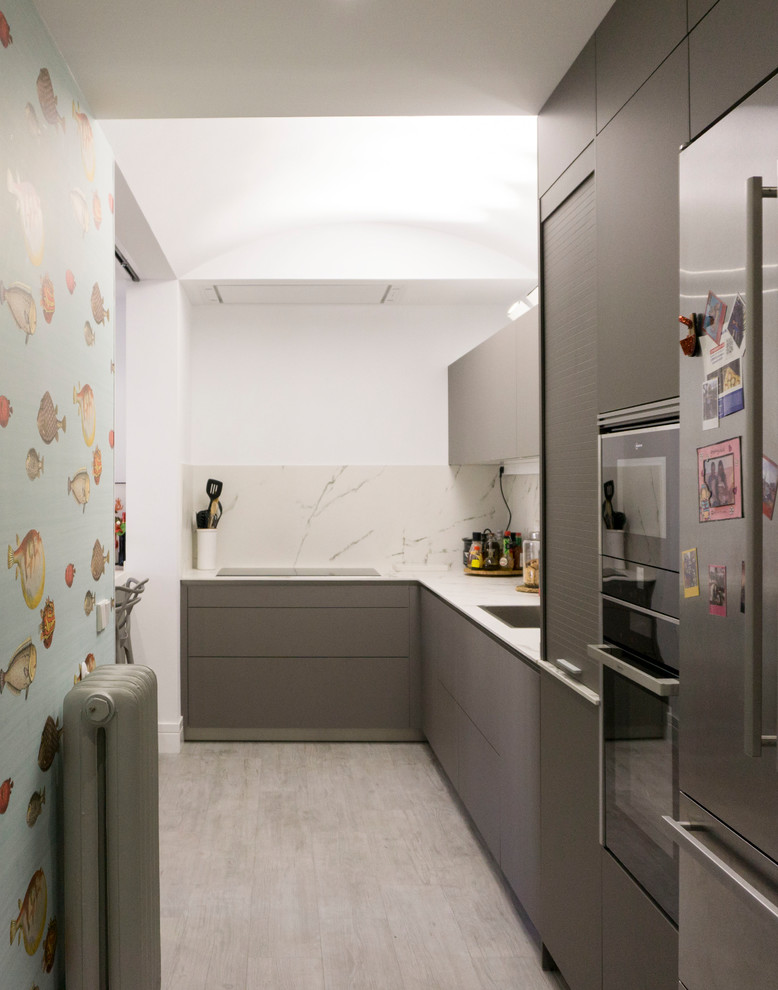 Photo of a mid-sized eclectic l-shaped open plan kitchen in Madrid with an undermount sink, flat-panel cabinets, grey cabinets, quartz benchtops, white splashback, marble splashback, panelled appliances, porcelain floors, a peninsula, grey floor and white benchtop.