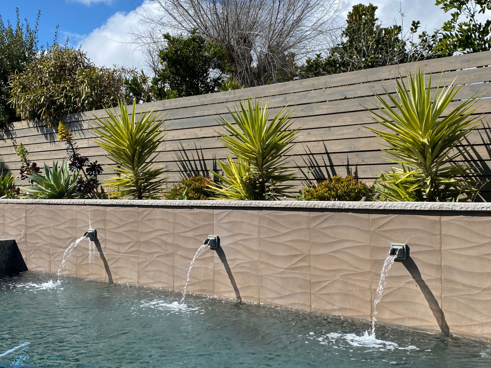 This is an example of a large contemporary backyard rectangular infinity pool in San Diego with with a pool and natural stone pavers.