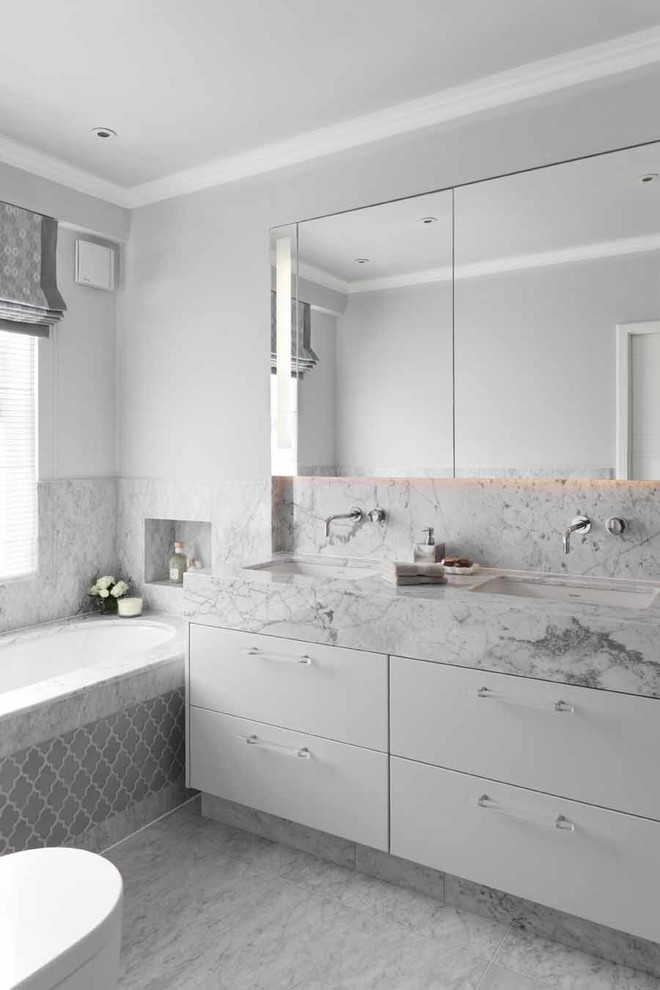 This is an example of a contemporary bathroom in London with an undermount sink, flat-panel cabinets, white cabinets, an undermount tub, gray tile and grey walls.