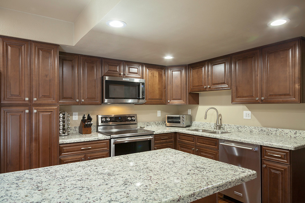 Mid-sized transitional l-shaped laminate floor and brown floor enclosed kitchen photo in Phoenix with an undermount sink, shaker cabinets, medium tone wood cabinets, granite countertops, multicolored backsplash, stone slab backsplash, stainless steel appliances and an island