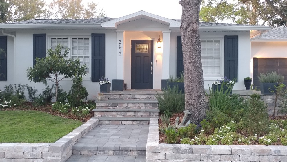 Photo of a mid-sized contemporary front yard partial sun driveway in Tampa with a retaining wall and concrete pavers.