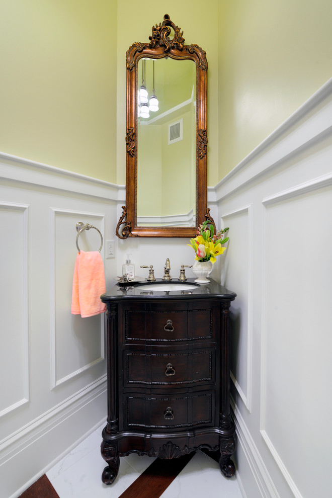 Inspiration for a small traditional powder room in St Louis with recessed-panel cabinets, dark wood cabinets, a two-piece toilet, yellow walls, marble floors, an undermount sink, solid surface benchtops, white floor and black benchtops.