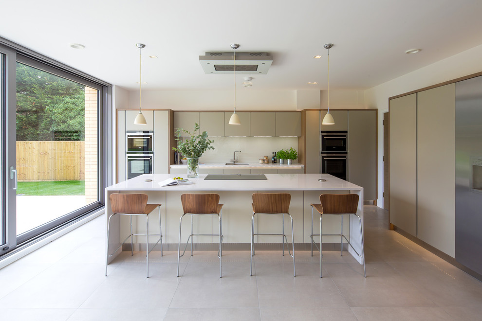 This is an example of a contemporary kitchen in Oxfordshire with an undermount sink, flat-panel cabinets, grey cabinets, white splashback, glass sheet splashback, black appliances, with island, beige floor and porcelain floors.