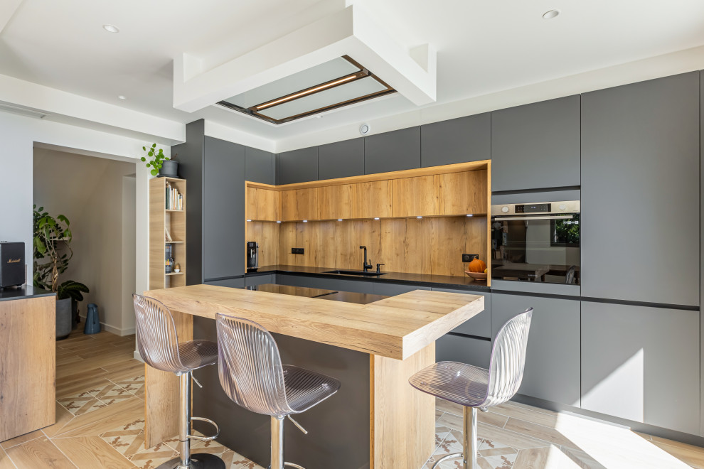 Photo of a mid-sized contemporary l-shaped open plan kitchen in Grenoble with an undermount sink, grey cabinets, granite benchtops, timber splashback, black appliances, ceramic floors, with island, beige floor and black benchtop.