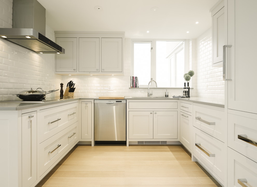 This is an example of a mid-sized transitional u-shaped eat-in kitchen in Vancouver with an undermount sink, shaker cabinets, grey cabinets, quartz benchtops, white splashback, ceramic splashback, stainless steel appliances, light hardwood floors and with island.