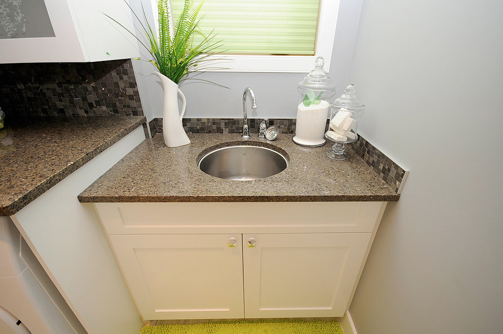 Photo of a mid-sized traditional single-wall utility room in Edmonton with an undermount sink, shaker cabinets, white cabinets, terrazzo benchtops, grey walls, a side-by-side washer and dryer, porcelain floors and beige floor.