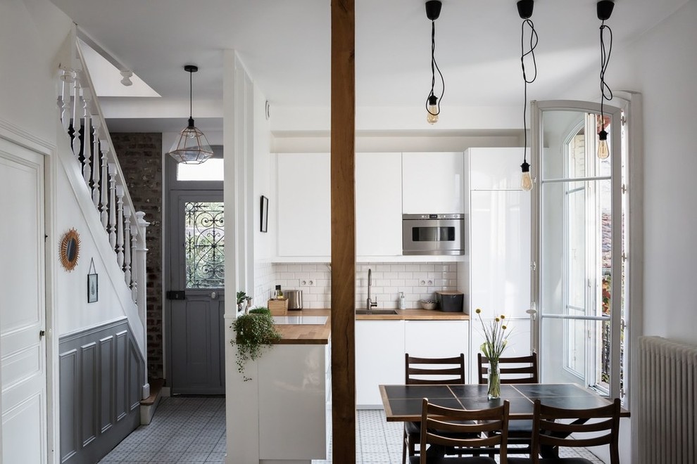 Small contemporary l-shaped eat-in kitchen in Paris with a single-bowl sink, flat-panel cabinets, white cabinets, wood benchtops, white splashback, subway tile splashback, stainless steel appliances, cement tiles, grey floor and no island.
