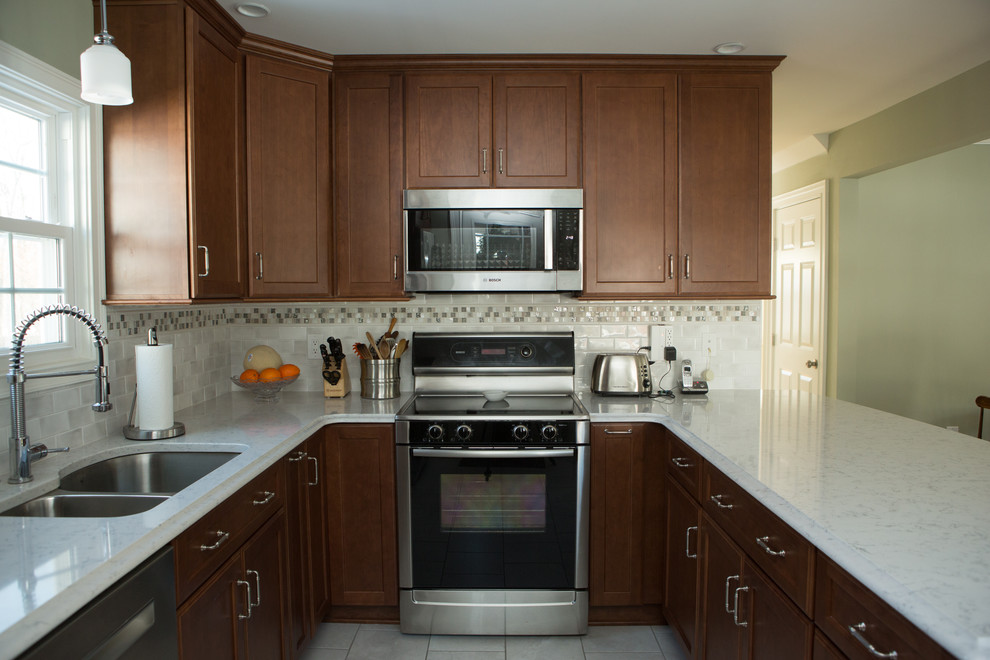 Example of a mid-sized transitional l-shaped white floor and ceramic tile eat-in kitchen design with an undermount sink, quartz countertops, white backsplash, stainless steel appliances, white countertops, shaker cabinets, medium tone wood cabinets, porcelain backsplash and a peninsula